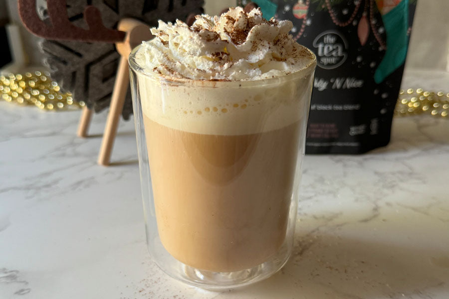 an eggnog tea latte in a glass mug sits in front of a tea bag and reindeer decoration