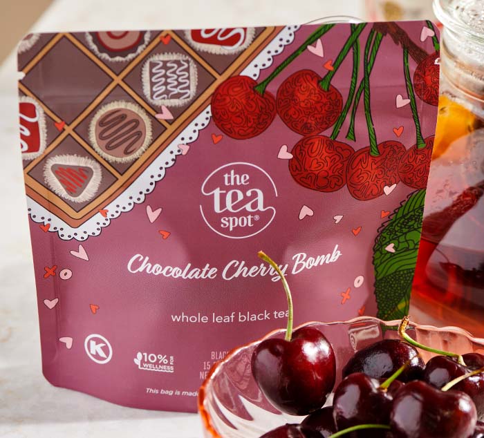 
                  
                    The image shows a close-up of The Tea Spot's Chocolate Cherry Bomb whole leaf black tea package, featuring cherries and chocolate imagery. In the background, there is a jar of brewed tea and fresh cherries placed on a light surface.
                  
                