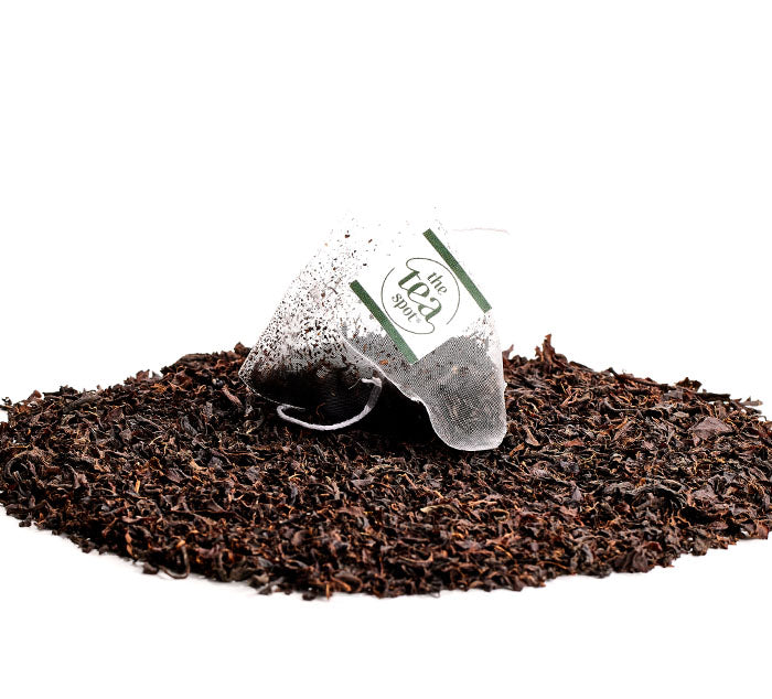 
                  
                    a tea bag sits atop a pile of black loose leaf tea leaves
                  
                