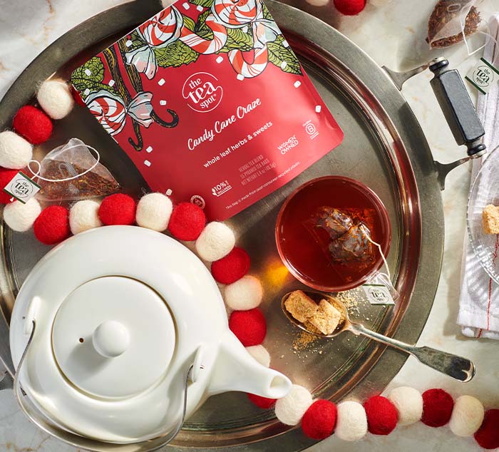 a red bag reading candy cane craze, whole leaf herbs and sweets sits on a tray with brewed tea and a tea pot