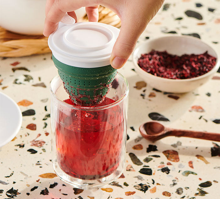 
                  
                    A hand lifting the green Tuffy Steeper from the Eclipse Mug, with hibiscus tea dripping into the double-walled glass mug below
                  
                