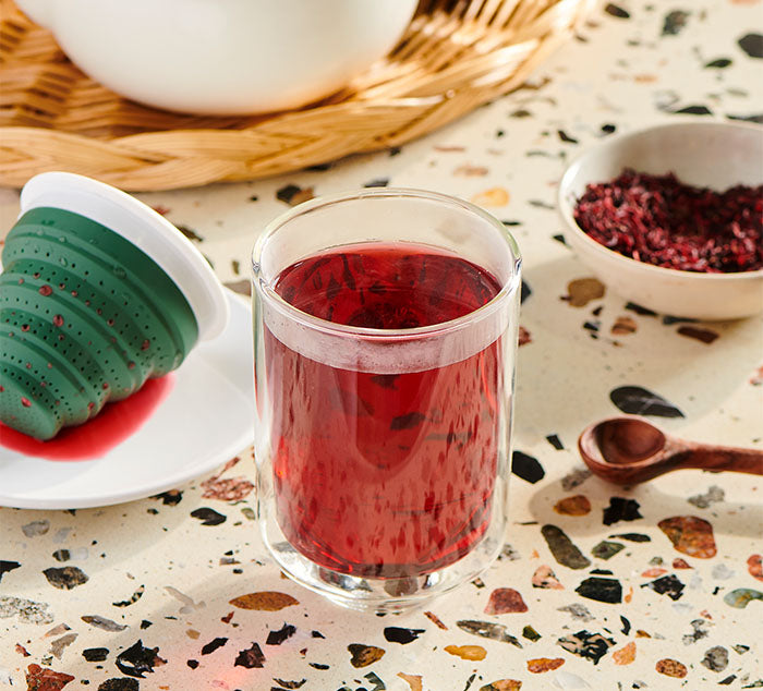 
                  
                    The Eclipse Mug filled with hibiscus tea, with the green Tuffy Steeper resting on a saucer beside it after steeping
                  
                