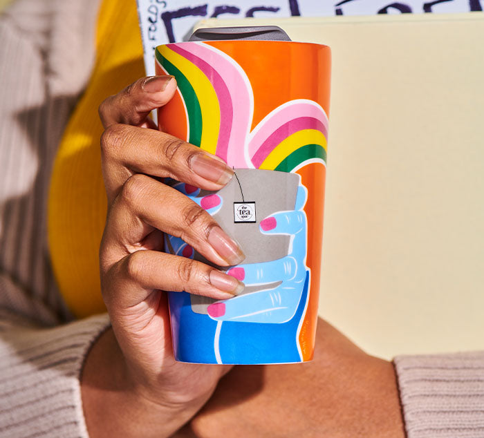 
                  
                    a mug with an image with rainbows and a tea cup is held by a person carrying folders
                  
                