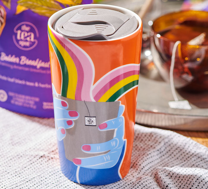 
                  
                    a ceramic travel mug is orange with rainbows and sitting on a table
                  
                