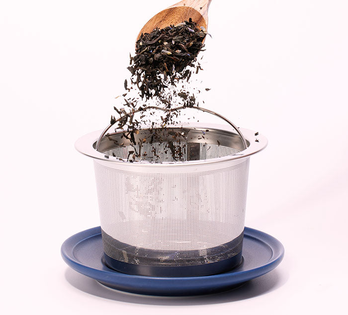 
                  
                    loose leaf tea leaves are poured into a large stainless steel infuser on top of a saucer
                  
                