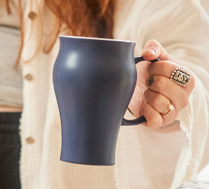 
                  
                    a person holds a dark blue ceramic mug in her hand
                  
                