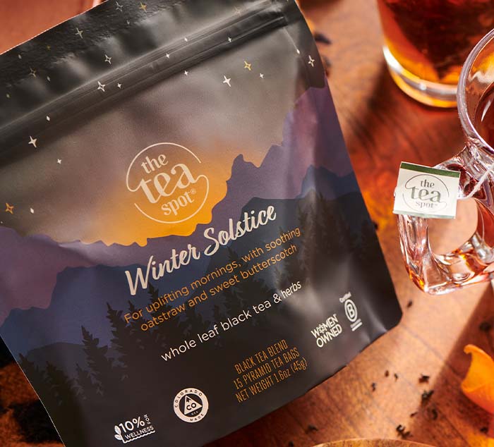 
                  
                    "Winter Solstice Tea pouch with its mountain and starry design, placed on a cozy wooden table alongside a clear glass mug of steeped tea, showcasing the inviting warmth and rich amber tones of the brew.
                  
                