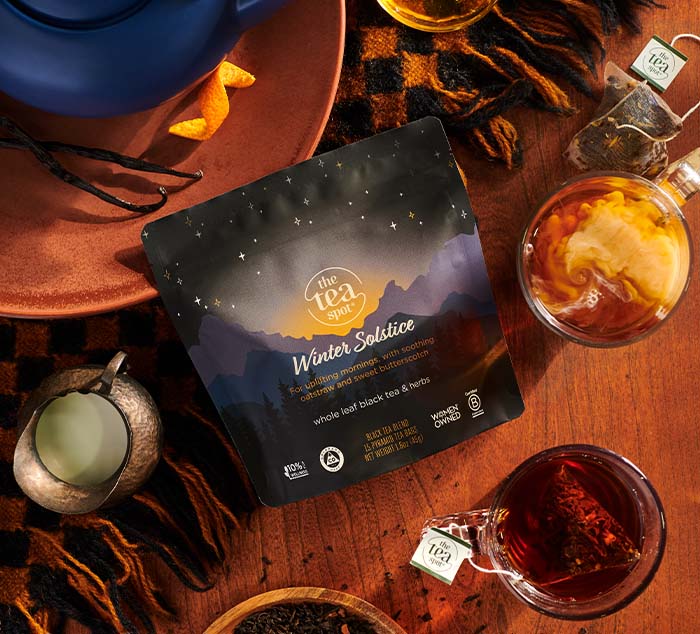 Winter Solstice Tea pouch displayed on a cozy winter setup with warm tones, featuring a teapot, a steaming cup of tea, and festive seasonal details like a blanket and milk pitcher.